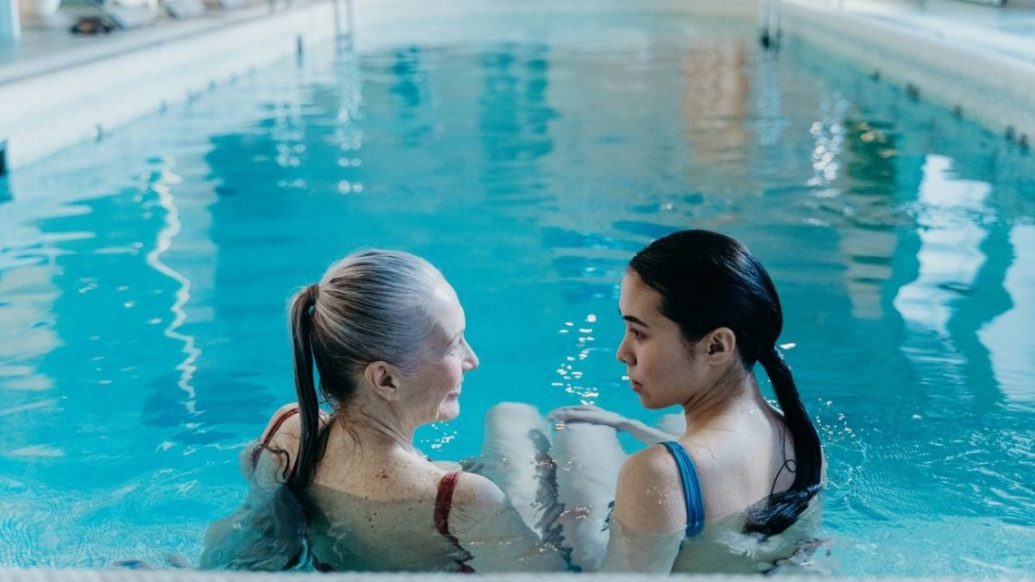 Elderly and young woman bonding in a serene indoor swimming pool environment.