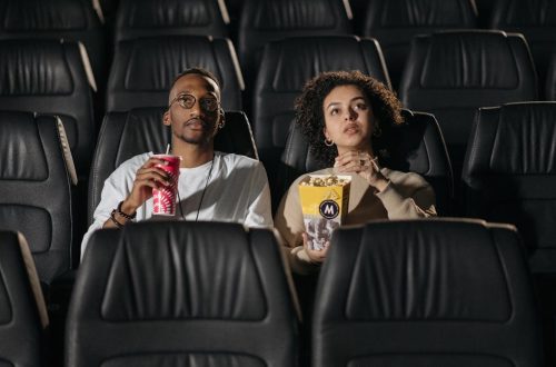 A couple sits in a cinema, enjoying popcorn while watching a movie.