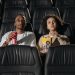 A couple sits in a cinema, enjoying popcorn while watching a movie.